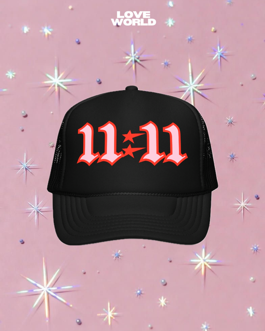 LOVE WORLD 11:11 Trucker Hat 2.0 product shot — black trucker hat with red and pink gothic 11:11 embroidery on sparkly pink background