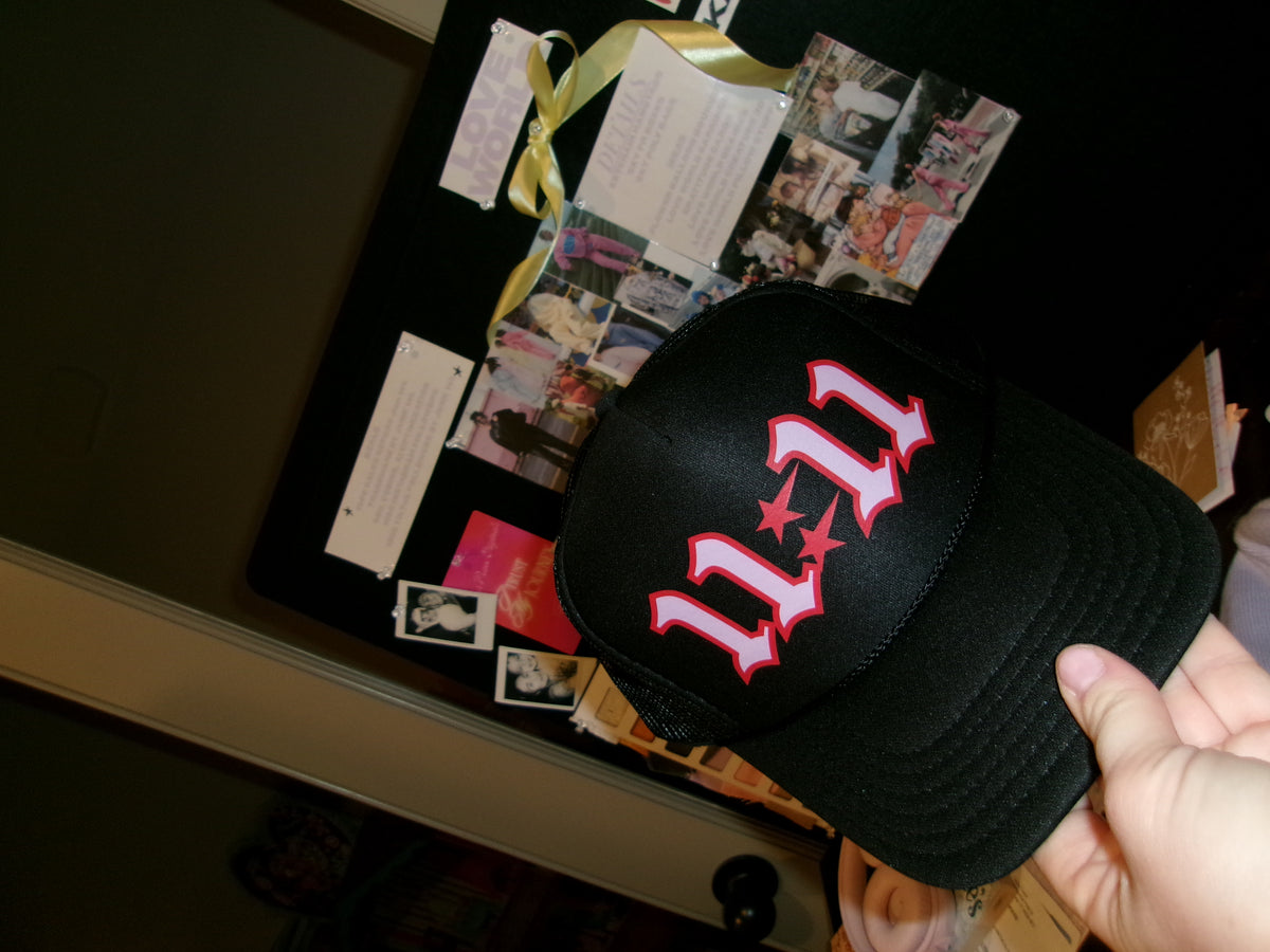 Close-up of the LOVE WORLD 11:11 Trucker Hat 2.0 — black structured front panel with bold red and pink 11:11 gothic lettering