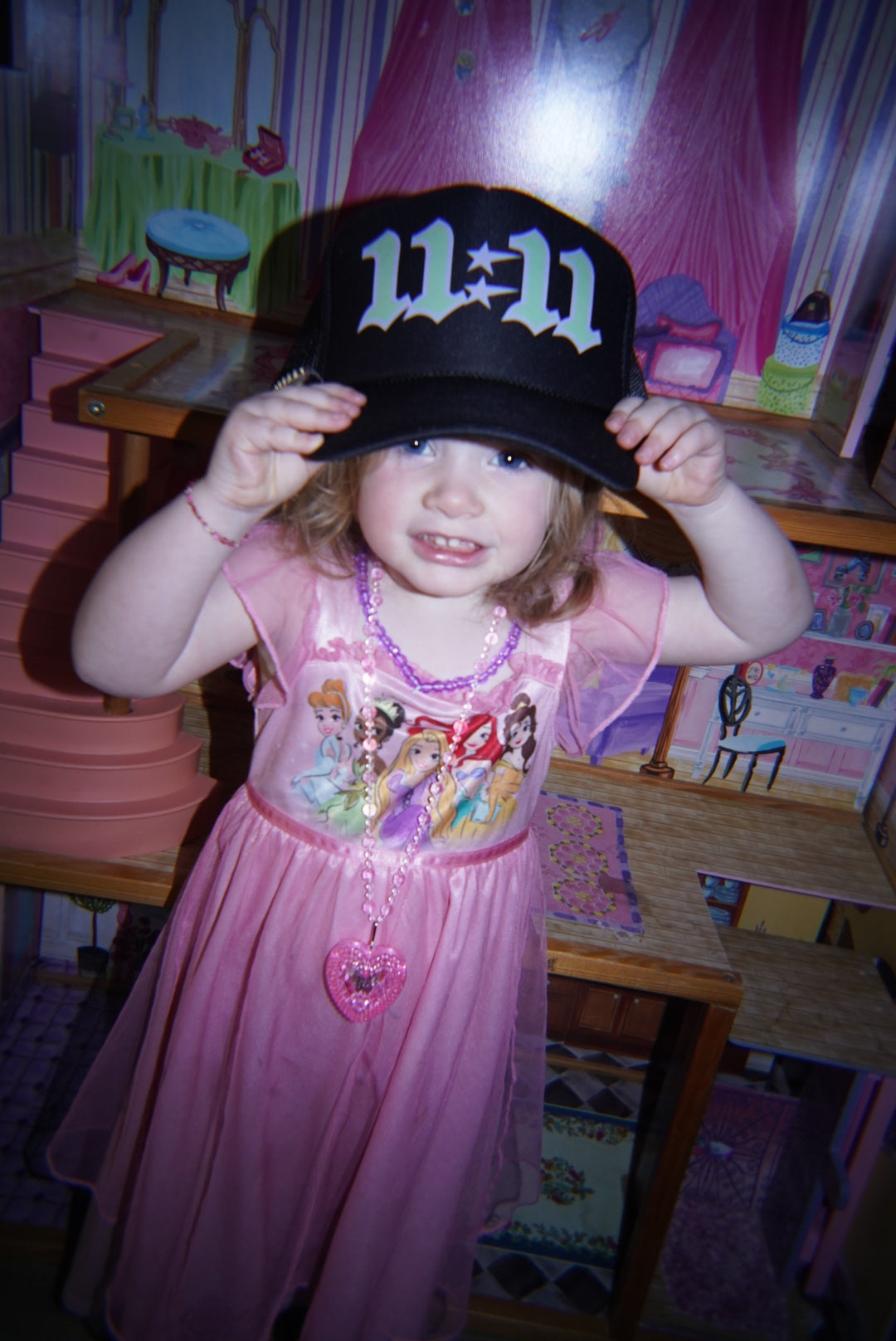 Little girl in a princess dress holding up the LOVE WORLD 11:11 Trucker Hat — black trucker with neon green gothic 11:11  dtf print