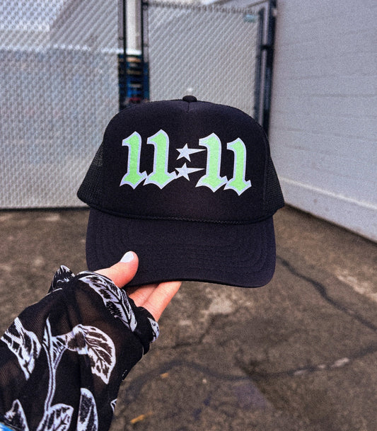 A person wearing a black trucker hat with the number 11:11 and a green graphic design on the front.Loveworldllc,Loveworldllc.com, mental health brand, mom brand, angel numbers,star hat, cool trucker hat,mother graphic tee, graphic designer, unique fashion, clothing brand, 1111,Pinterest outfit, self Love brand, mom brand,gifts for her, gifts for mom