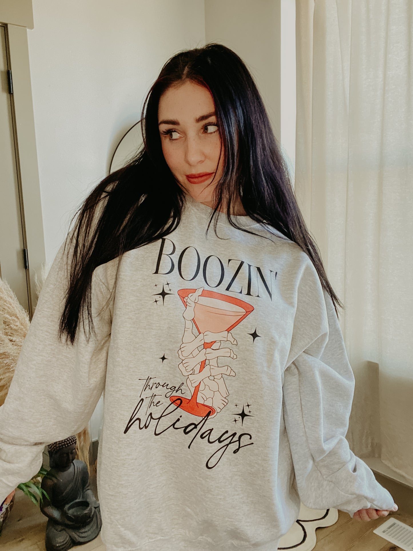 This image features a cozy, gray crewneck sweatshirt adorned with a playful and festive design, perfect for the holiday season. The front of the sweatshirt displays a whimsical illustration of a character holding a mug, with the humorous text, "From my experience, the holidays are.