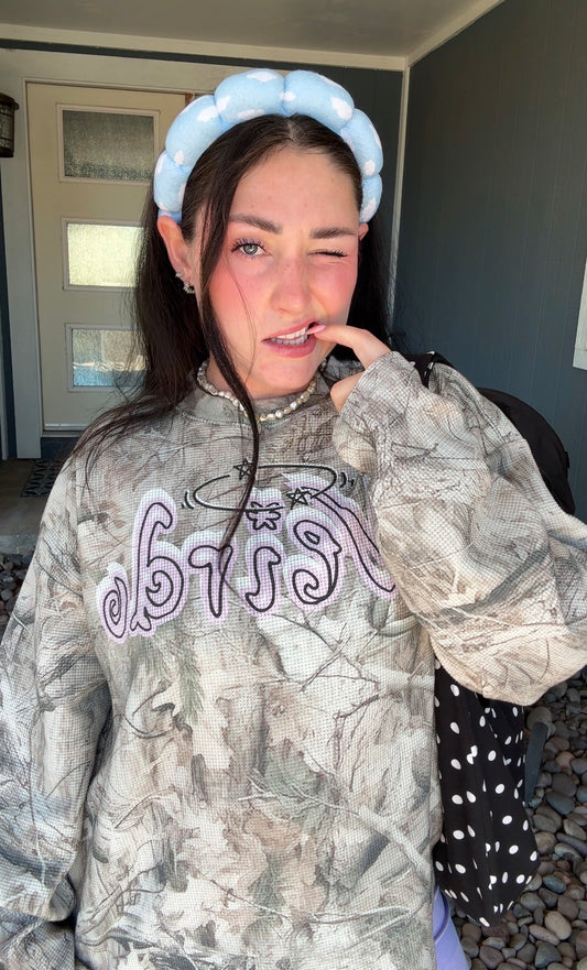 Model wearing LOVE WORLD’s oversized Weirdo tree camo long sleeve with lilac shorts and gray star cowboy boots.