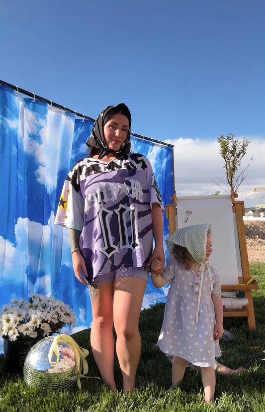 Two women standing outdoors with a blue sky and white clouds in the background.