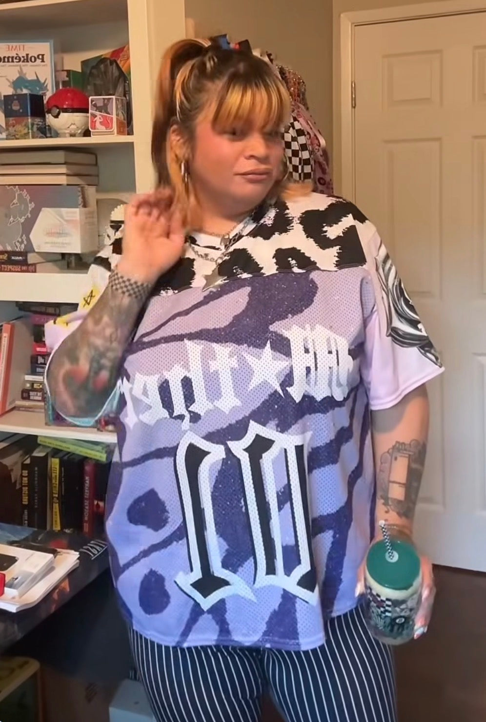 A woman wearing a purple and black camouflage mother jersey,with white gothic lettering, paired with black and white striped pants
