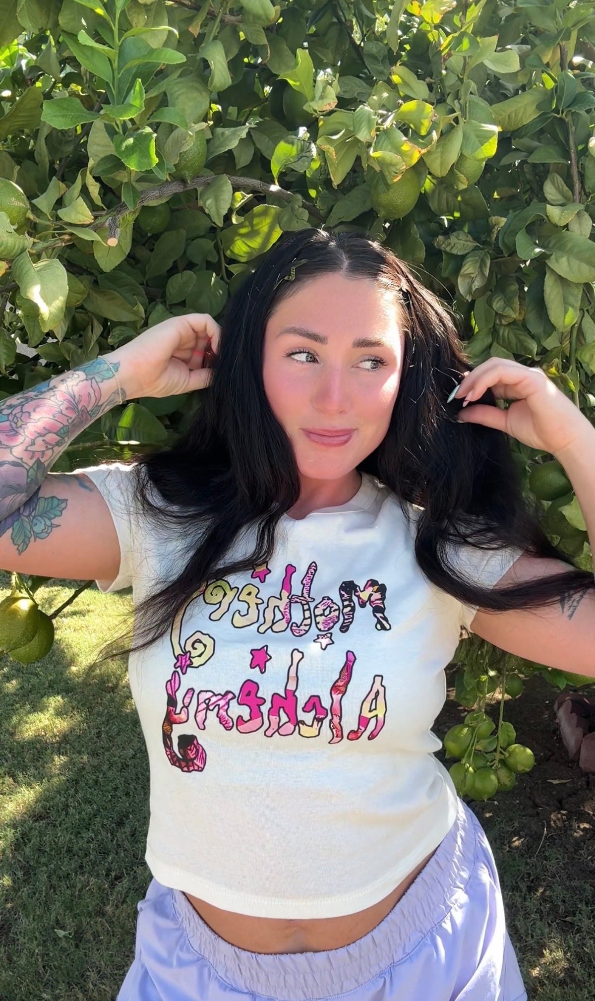 Close-up of woman wearing the Mothers Alchemy cropped tee — pink and yellow graphic on natural blend