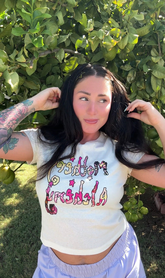 Close-up of woman wearing the Mothers Alchemy cropped tee — pink and yellow graphic on natural blend