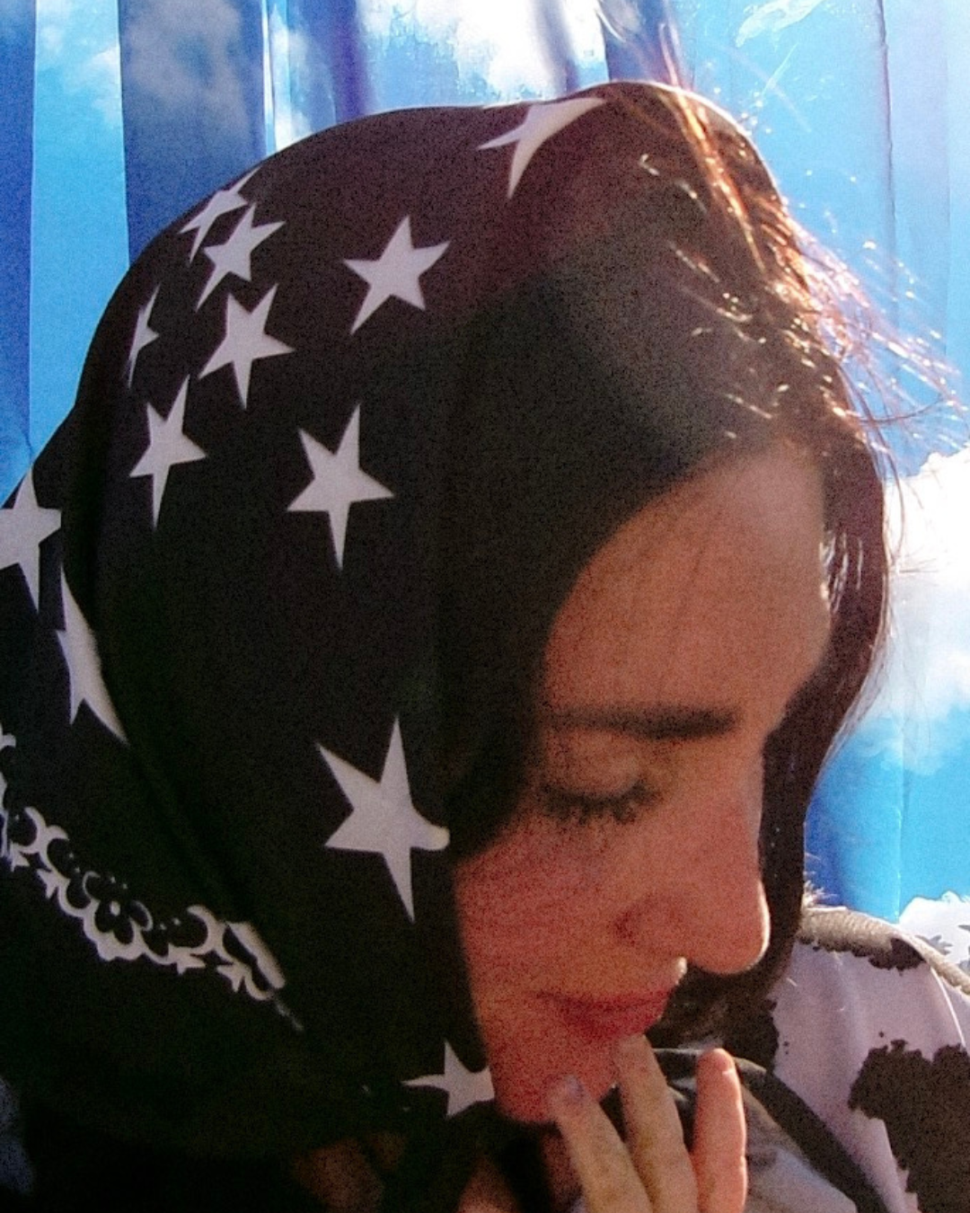 A close-up lifestyle shot of a woman wearing a black headscarf with a white star pattern, set against a bright blue background,womens graphic jersey, jersey for women, trendy top for women, womens clothing brand, dopamine dressing,dopamine clothing brand, t-shirt with a colorful graphic reading mother with snakeskin and leopard design, loveworldllc.com, stars and leopard jersey for women, pinterest ootd, star bandana